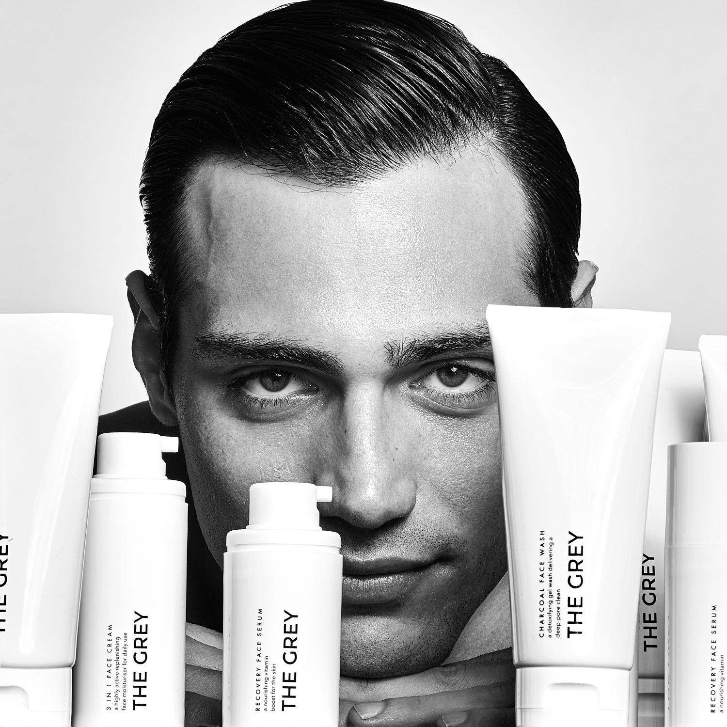 Close-up of a man surrounded by the grey men's skincare products including face washes and serums