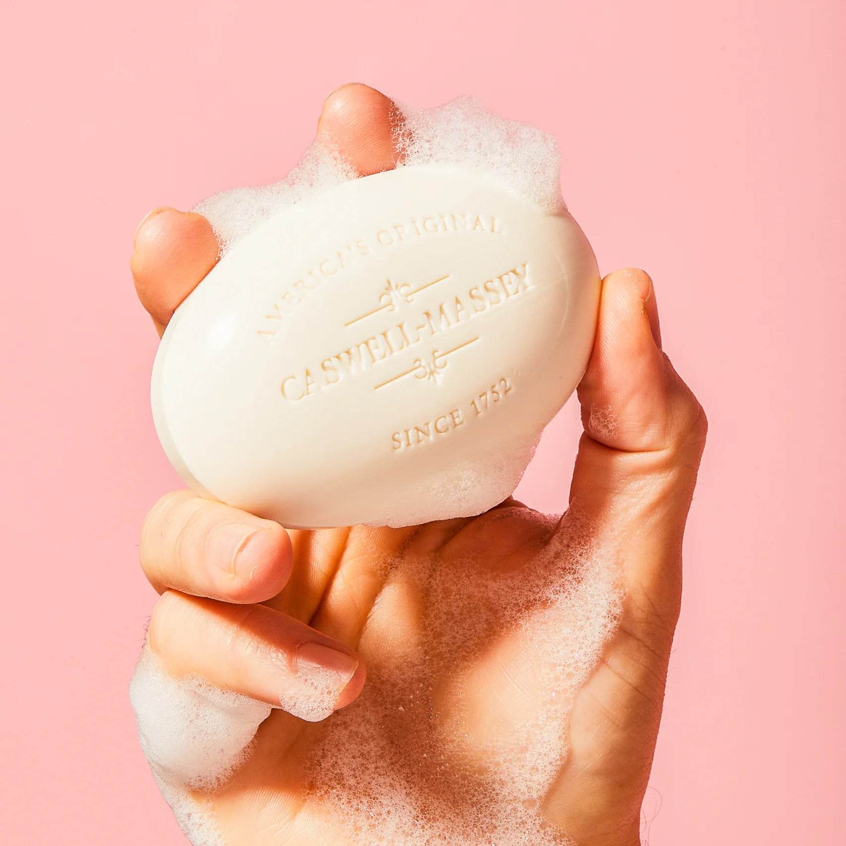 Hand holding a lathered Caswell-Massey soap bar, representing bath and body care products