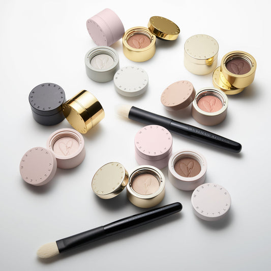 Makeup products including compact powders and brushes on a light background