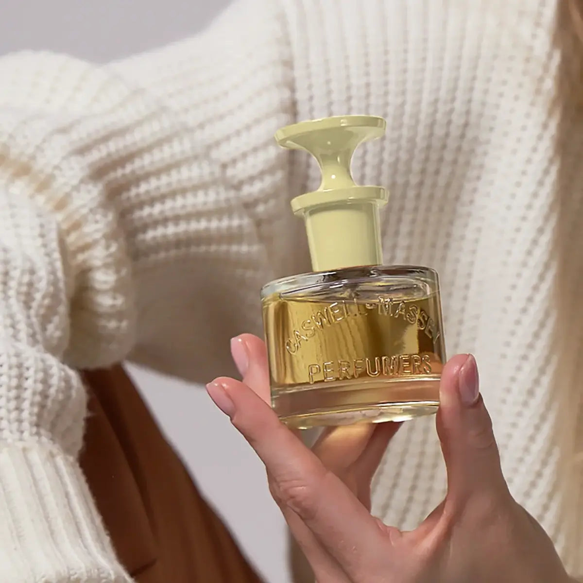 Person holding a perfume bottle with text 'Fragrance for Women' on a neutral background