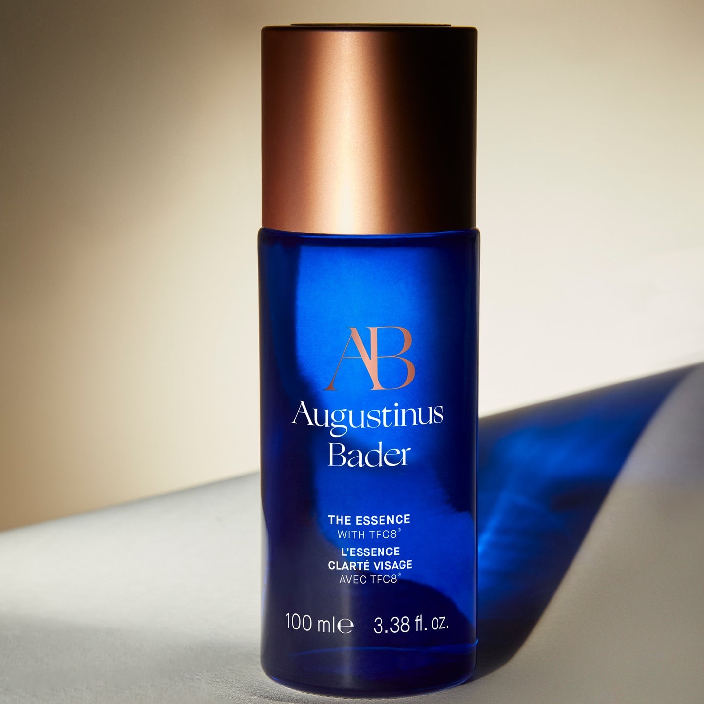 Augustinus Bader The Essence skincare product in a blue glass bottle with a copper lid, 100 ml