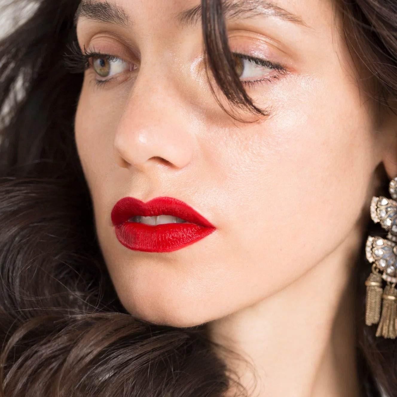 Close-up of woman wearing Madame Gabriela lipstick shade Paris At 7pm with red matte finish and statement earrings