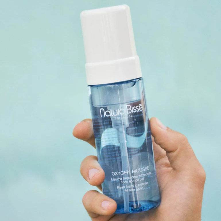 Natura Bisse Fresh Foaming Cleanser Oxygen Mousse in a clear blue bottle with white cap held in hand