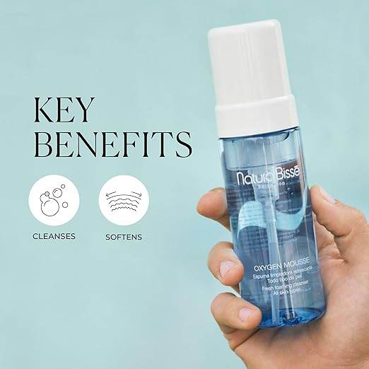Natura Bissé Fresh Foaming Cleanser Oxygen Mousse in blue bottle held in hand highlighting key benefits cleansing and softening