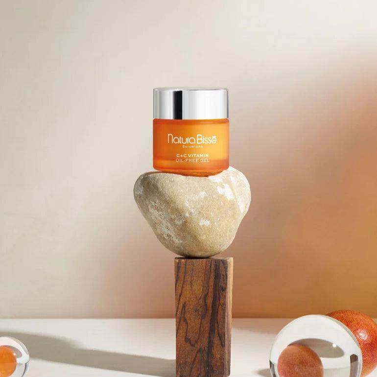 Natura Bisse lightweight firming moisturizer in an orange jar with silver lid displayed on a balanced stone and wooden block