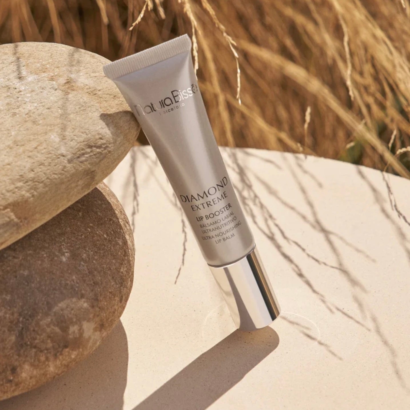 Natura Bisse Nourishing Lip Serum Diamond Extreme Lip Booster tube resting on natural stones outdoors