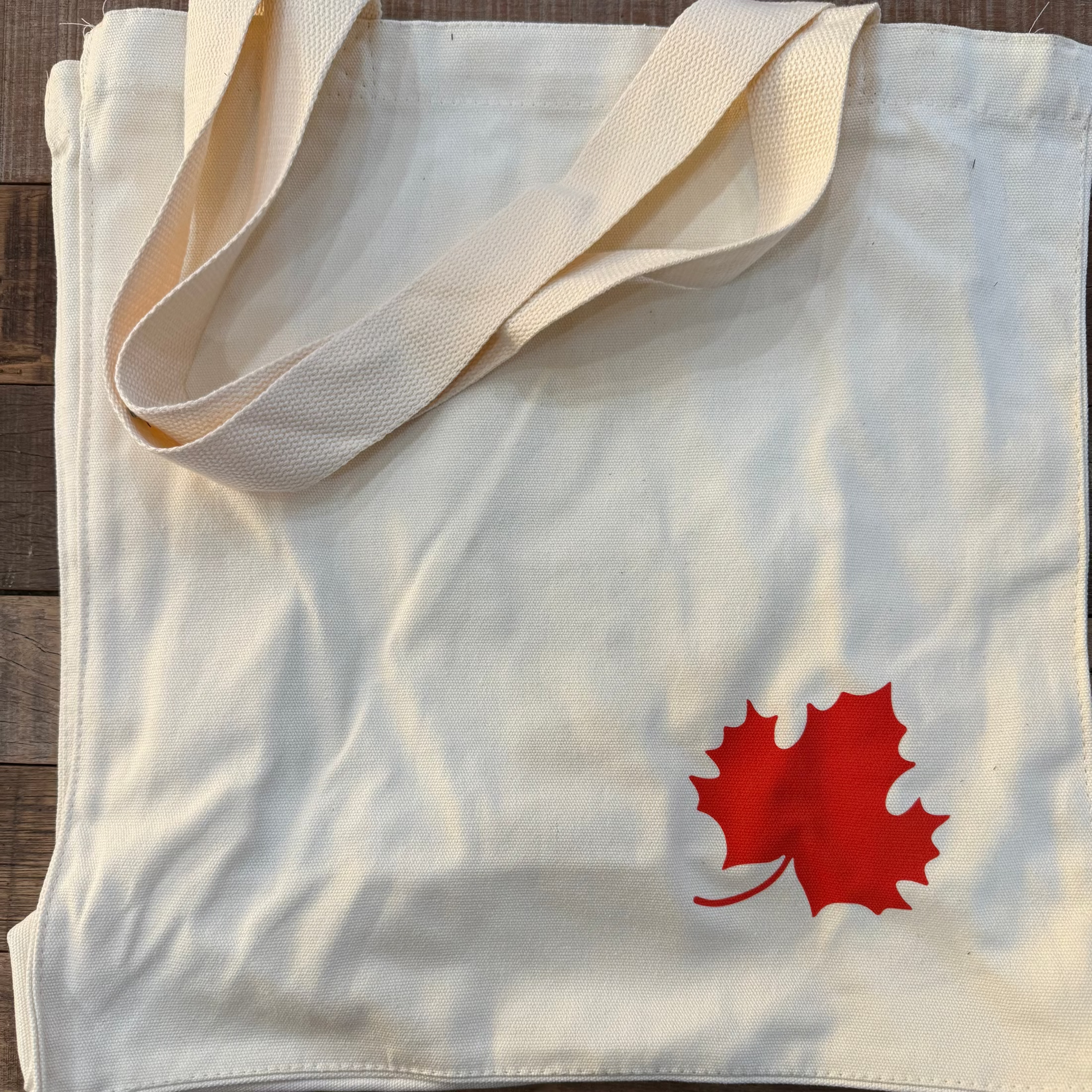 White tote bag with a red maple leaf design on a wooden surface