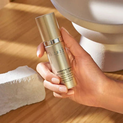 Hand holding a skincare bottle on a wooden surface with a blurred background