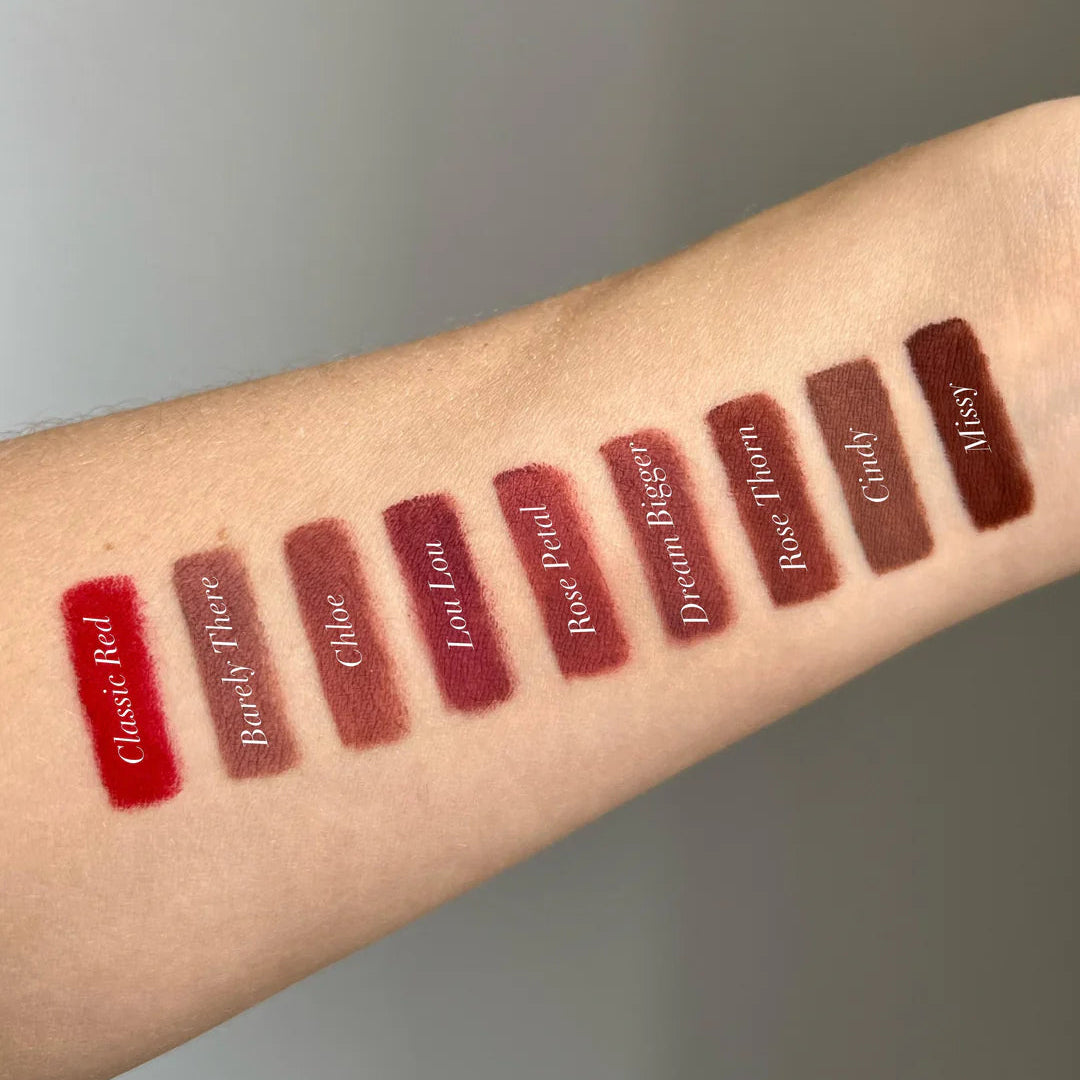 Lipstick swatches on a person's arm with color names underneath against a neutral background