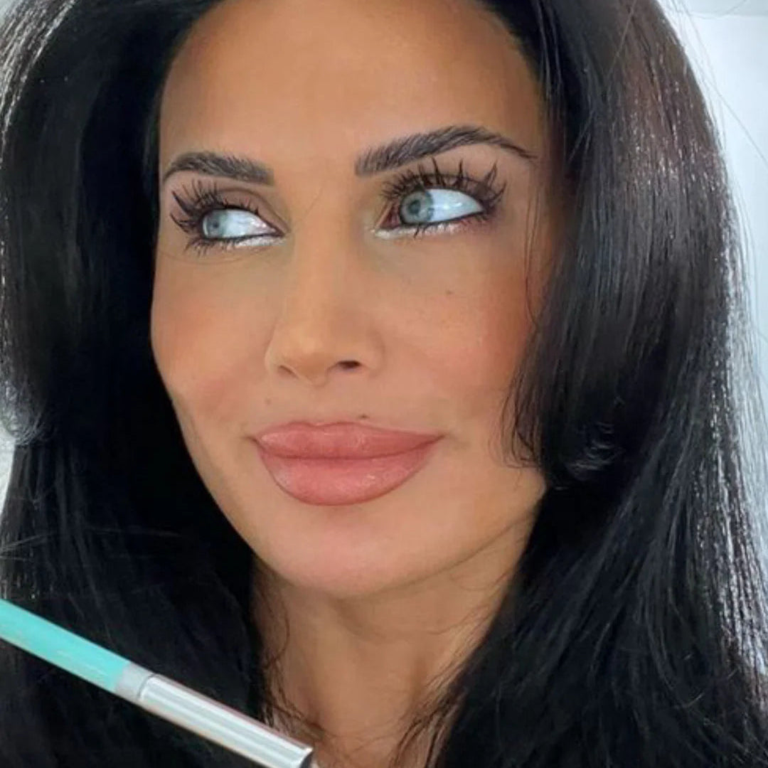 Woman with makeup brush near face against a neutral background