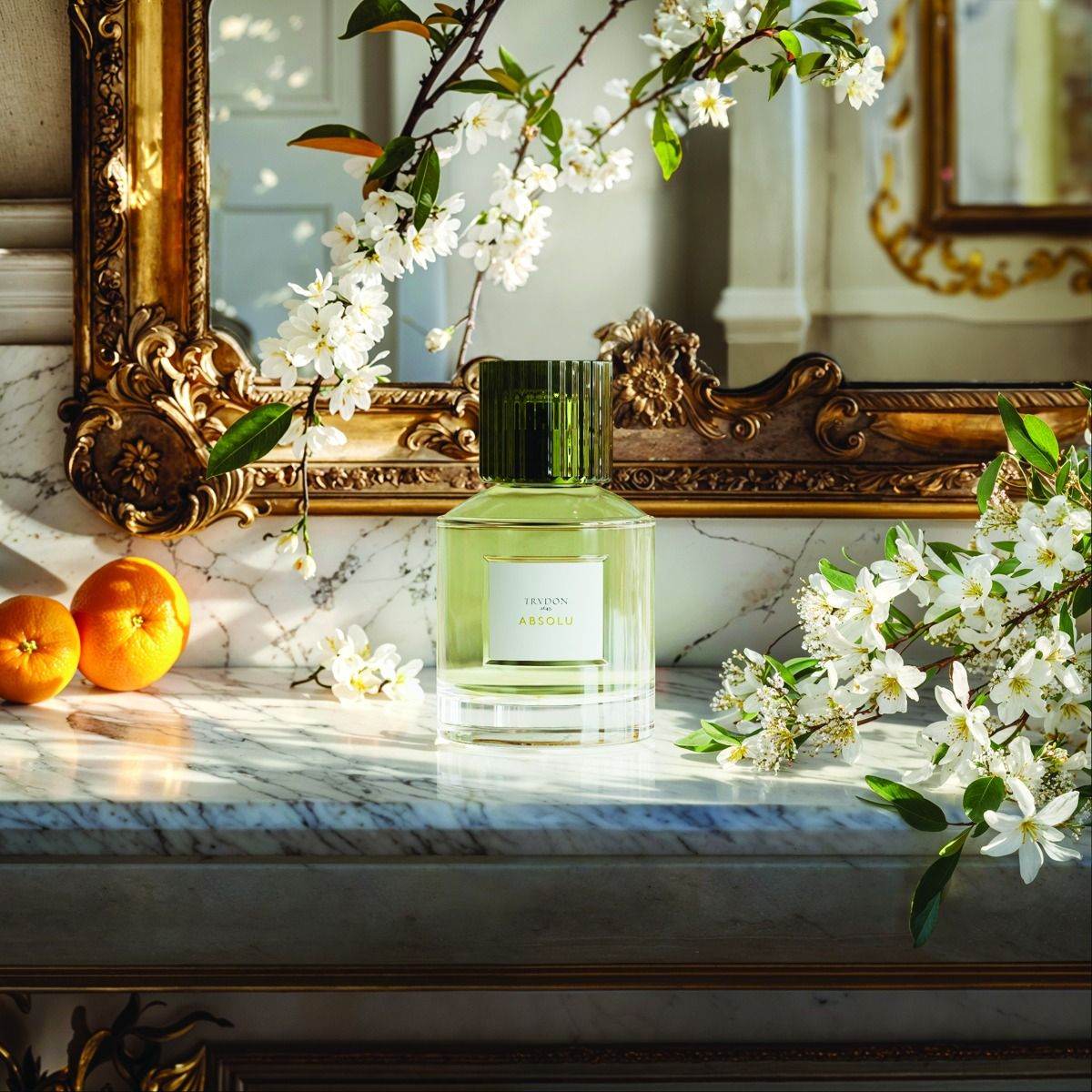 Trudon Absolu Eaux de Parfum displayed on a marble countertop with orange fruits and floral accents