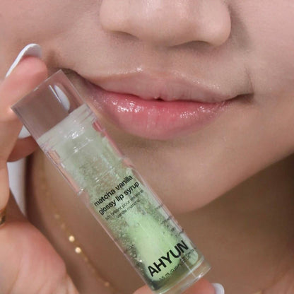 AHYUN matcha vanilla lip gloss held near model lips showing sheer green glossy finish