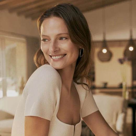 Natura Bisse Firming Serum displayed with a smiling woman showcasing youthful skin and healthy glow