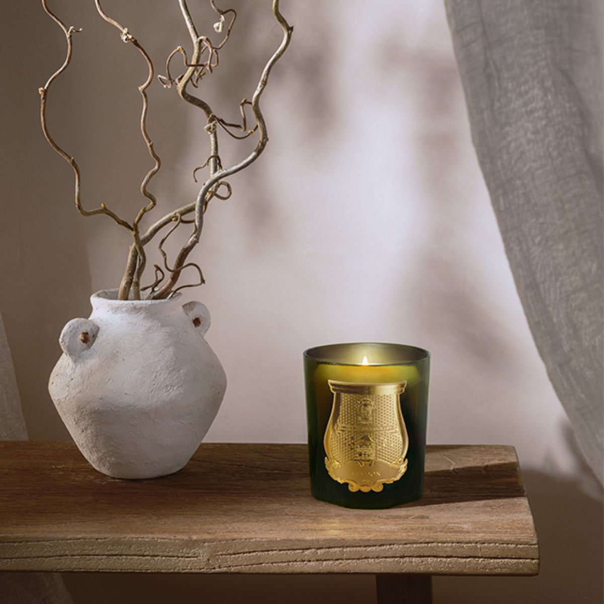 Trudon Cyrnos Candle in a green glass holder with elegant gold detailing, placed on a wooden table