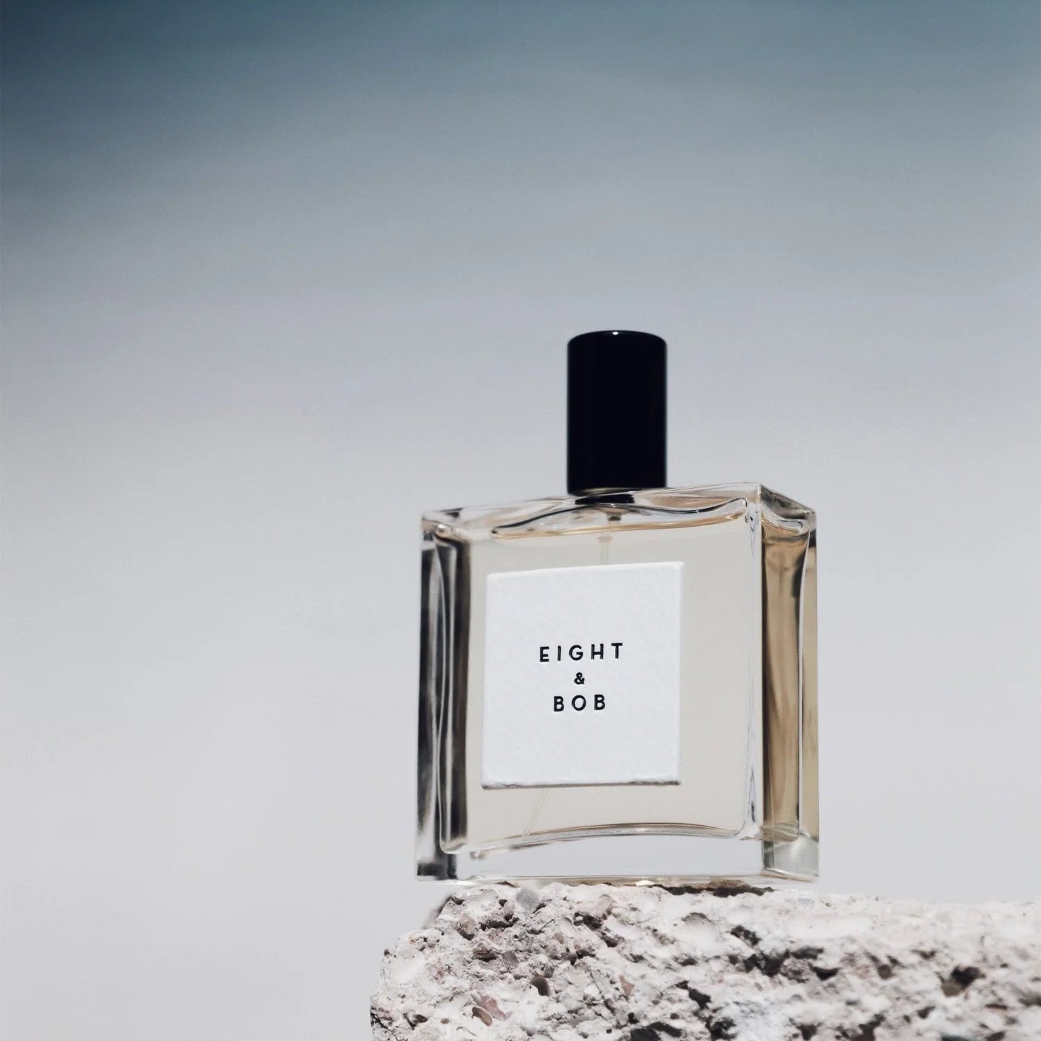 Eight & Bob perfume bottle The Original fragrance with clear glass and black cap on textured stone