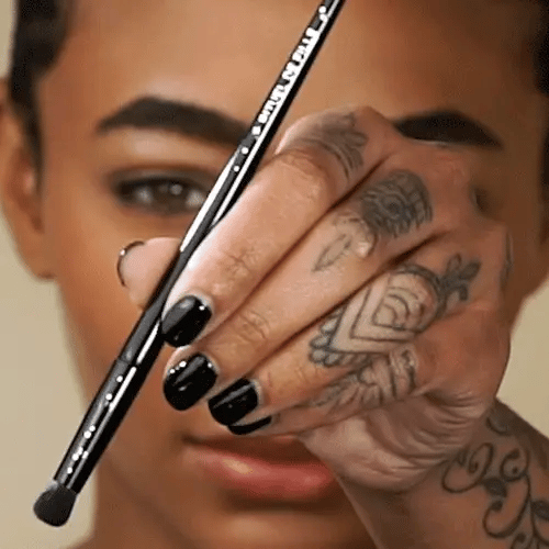 Rituel de Fille Eyeshadow Brush held by a person with elegant tattoos for precise makeup application