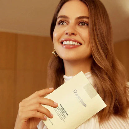 Natura Bissé Plumping And Firming Mask held by a smiling woman with healthy skin in a serene setting