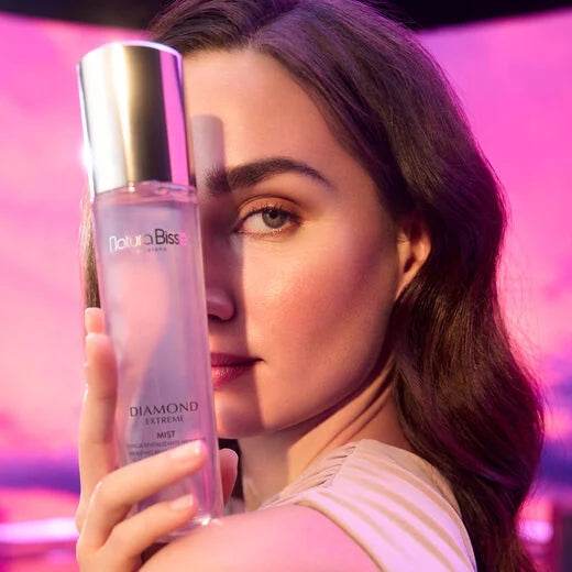 Natura Bissé Hydrating Revitalizing Essence in a sleek bottle held by a woman with glowing skin