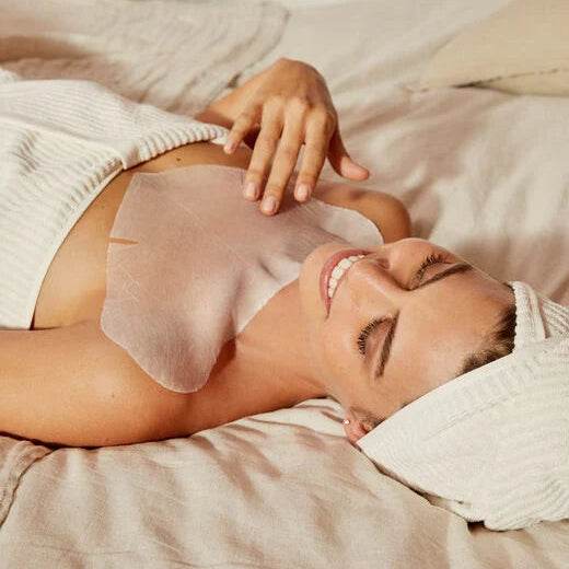 Natura Bissé Neck Mask applied on a smiling woman relaxing on a bed with a towel on her head