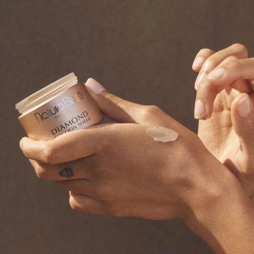 Natura Bisse Diamond Tinted Moisturizer displayed on a hand, showcasing a rich, hydrating formula