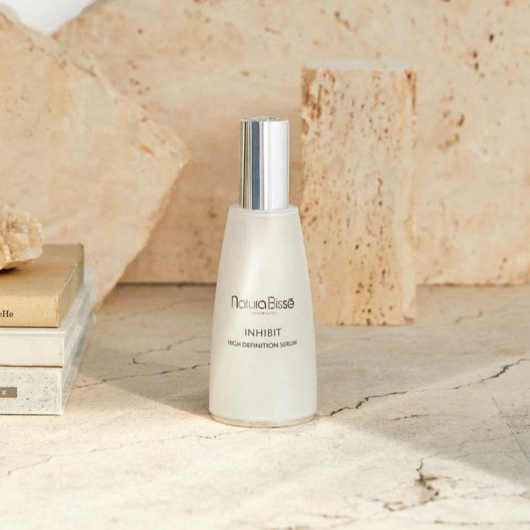 Natura Bisse Inhibit Firming Serum Bottle on a Natural Stone Surface