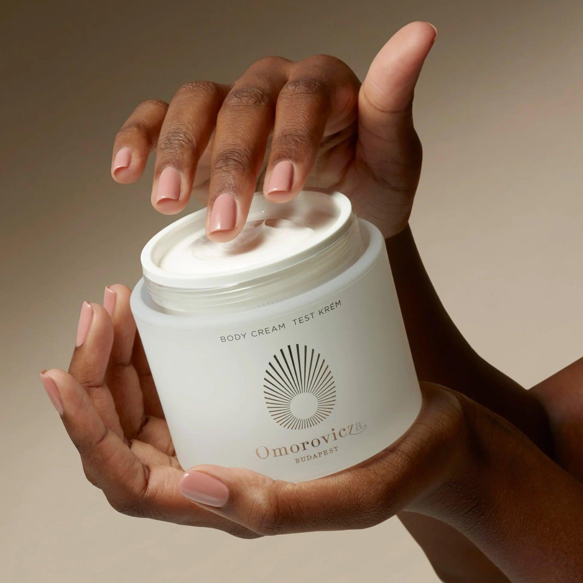 Omorovicza Body Cream in a frosted jar with a smooth texture being held by hands