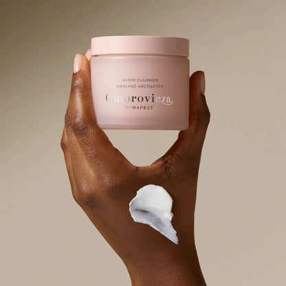 Omorovicza Queen Cream Cleanser in a pink jar held in hand, showcasing creamy texture on skin