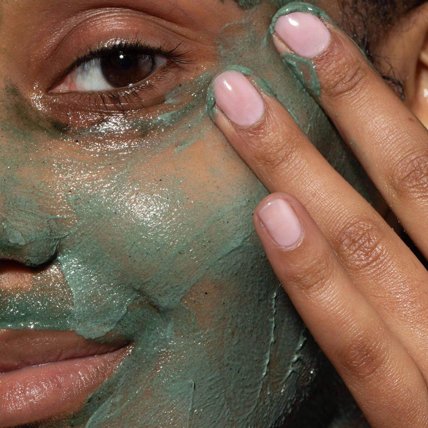 Close-up of a woman using Omorovicza Facial Polisher with green exfoliating mask on her skin