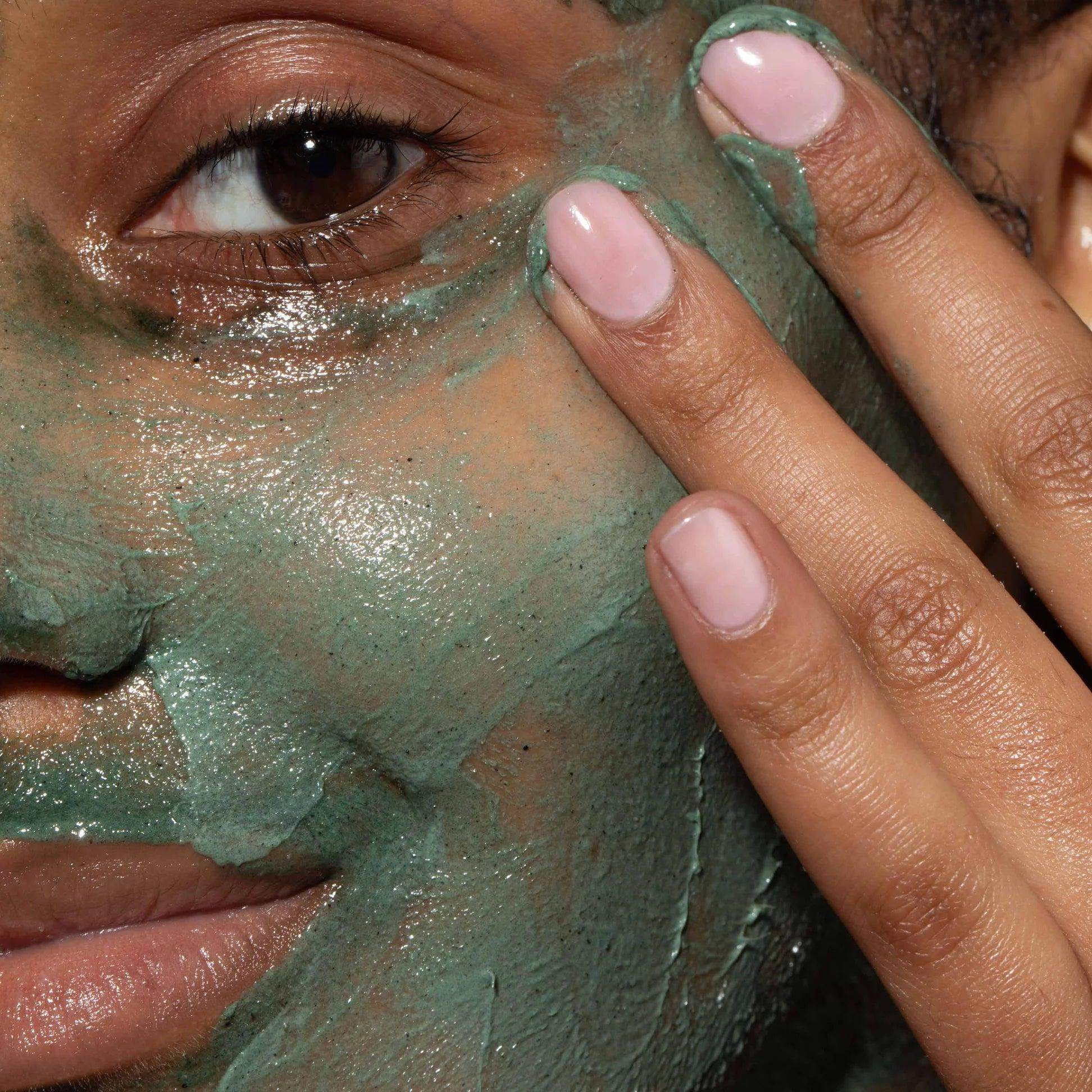 Close-up of a woman using Omorovicza Facial Polisher with green exfoliating mask on her skin
