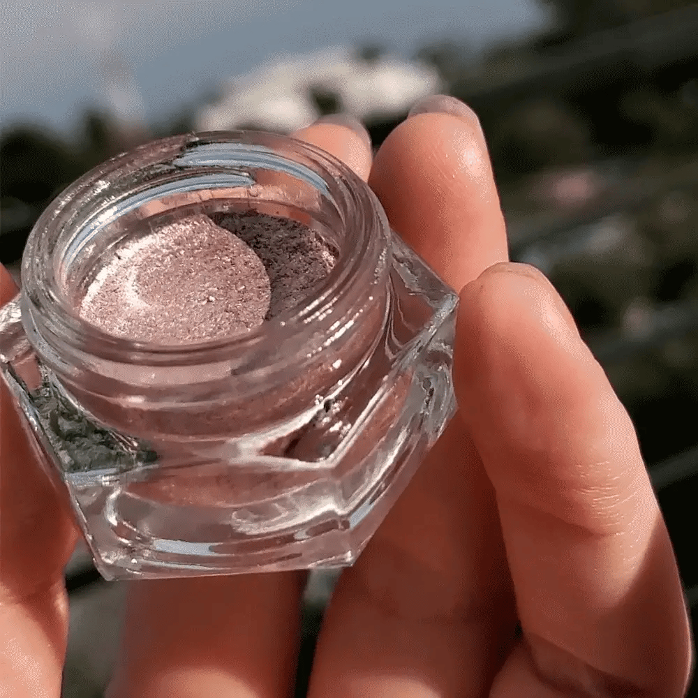 Rituel de Fille Cream Eyeshadow in a clear jar, showcasing a shimmering mauve shade held in a hand