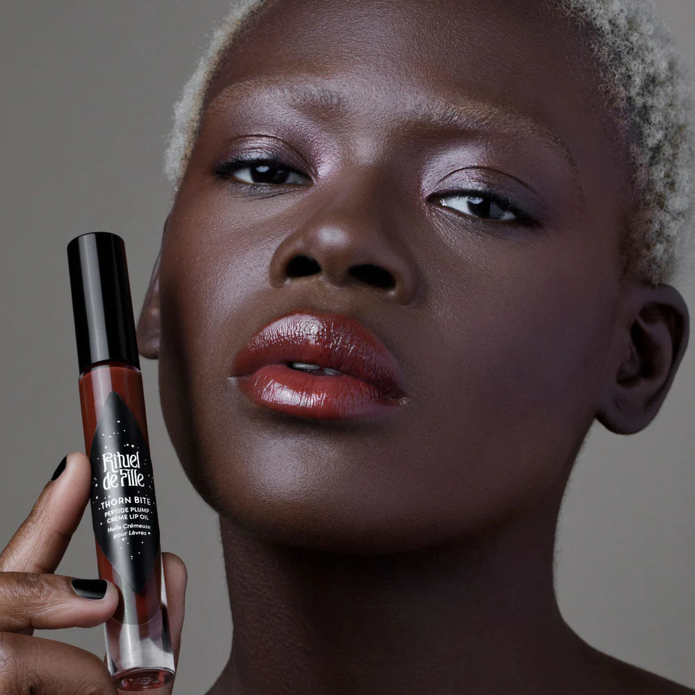 Rituel de Fille Lip Oil in a sleek packaging, applied on model's lips for a glossy finish