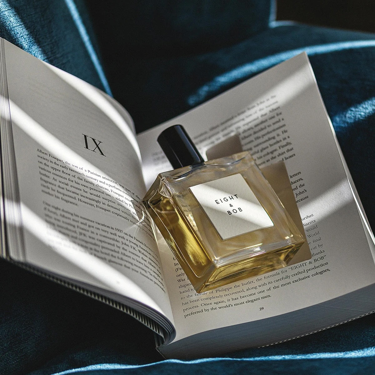 Eight & Bob The Original fragrance bottle placed on an open book in natural light