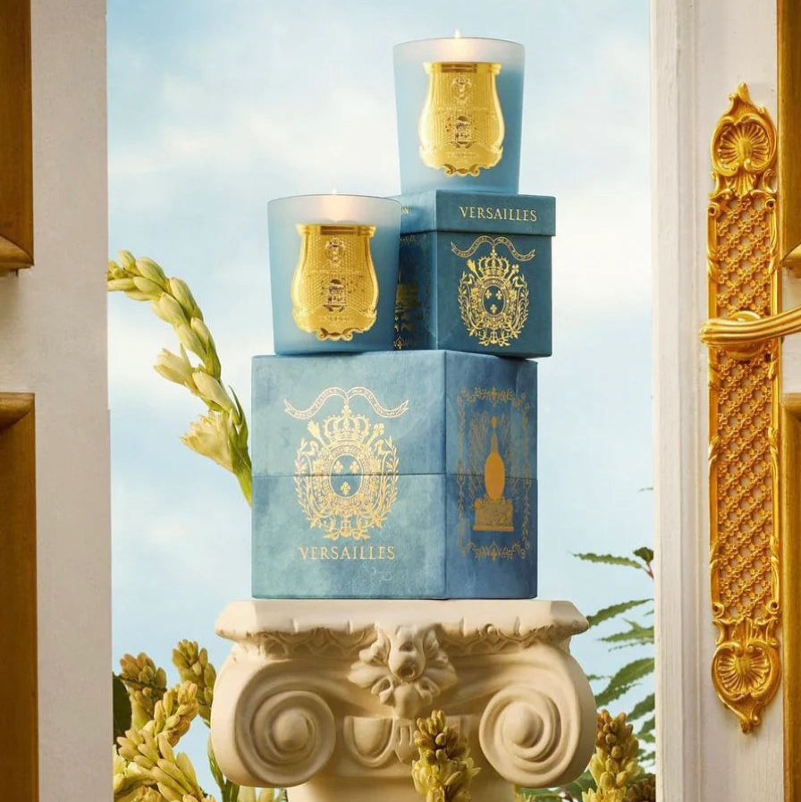London Beauty Versailles Candle set in blue and gold packaging displayed on ornate pedestal with floral background