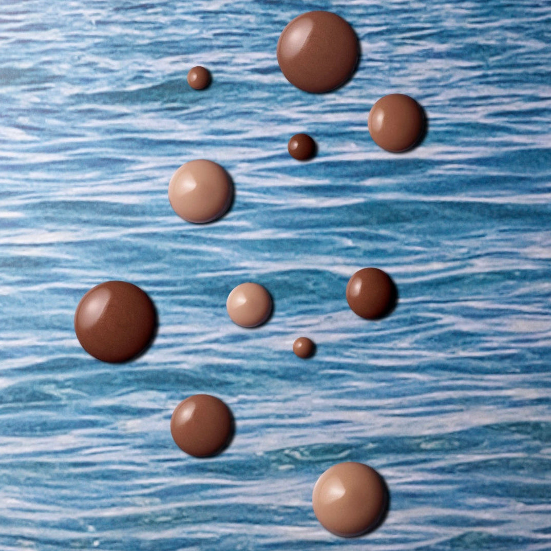 Westman Atelier Liquid Bronzer drops in various shades on a blue background for a sun-kissed glow